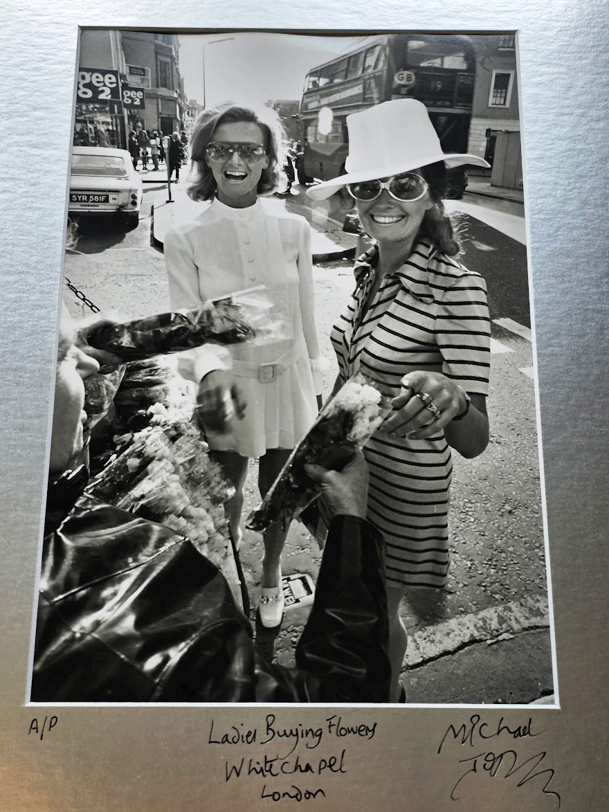 Carefree sixties London ladies buying flowers, bus and Gee 2 shop in background by Michael Joseph