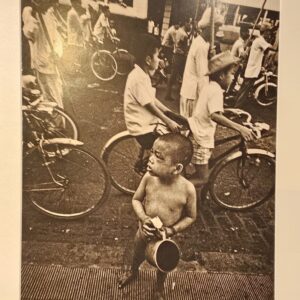 South Vietnam, boy begging in street while world carries on around him by Michael Joseph