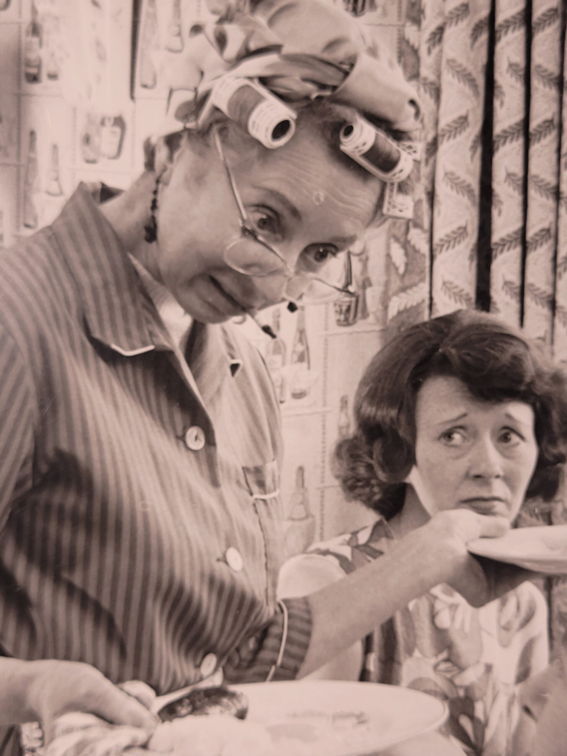 Family meal, housewife serving bangers and mash in curlers stereotypical british sixties household, by Michael Joseph