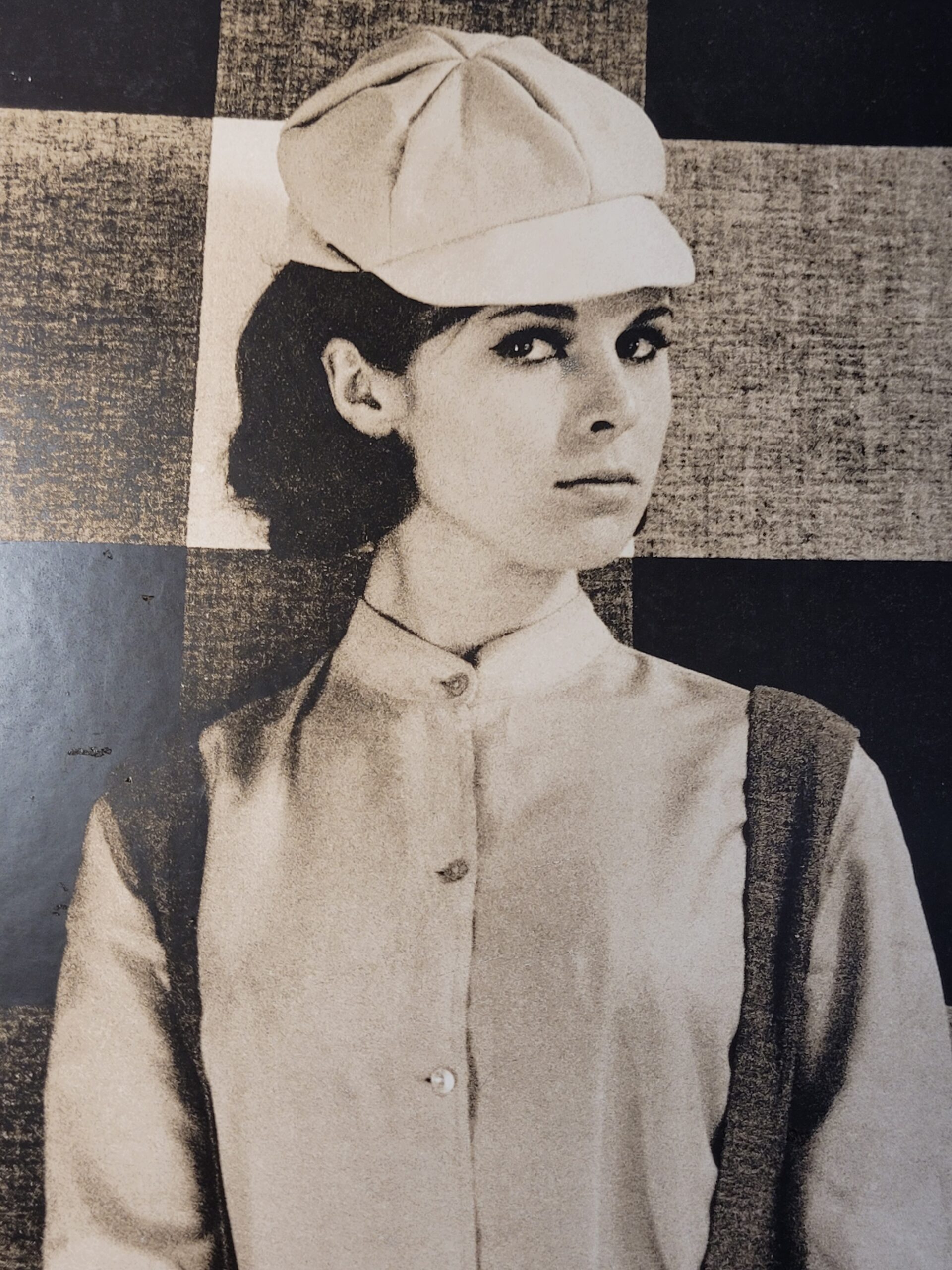 Pretty brunette with hat in front of geometric wallpaper, by Michael Joseph