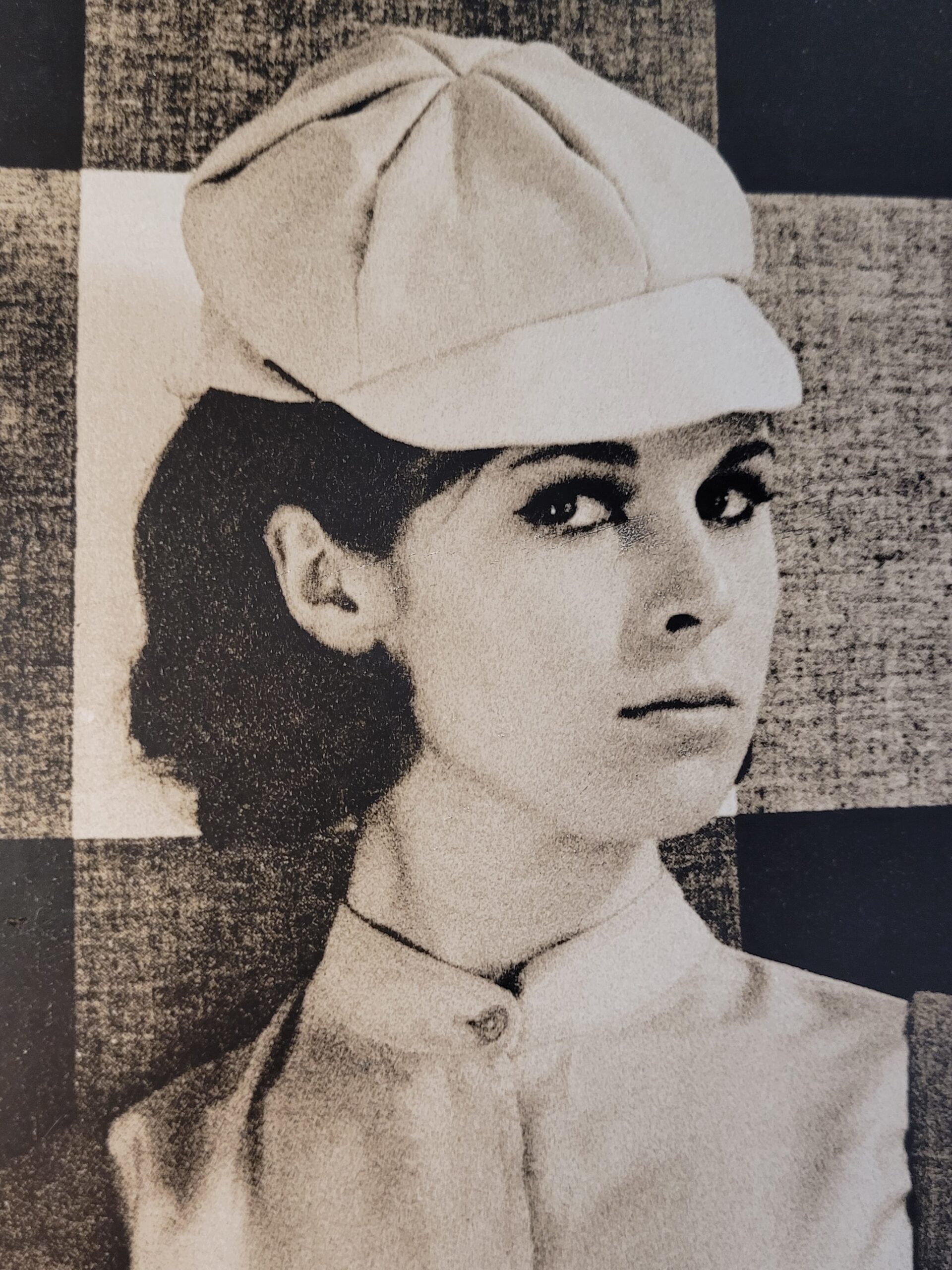 Pretty brunette with hat in front of geometric wallpaper, by Michael Joseph