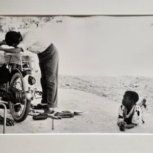 Child lying on floor watching motorbike reparation by Michael Joseph