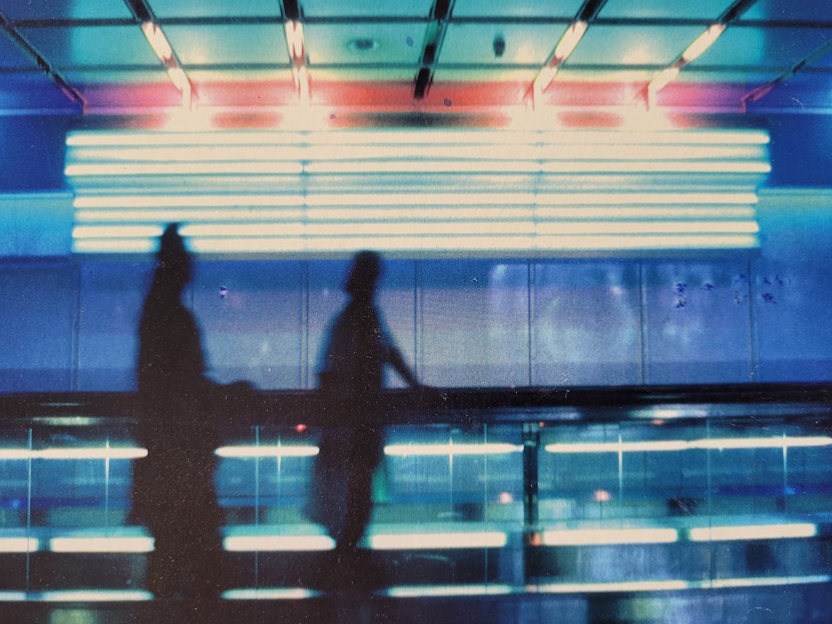 Silhouette d'un couple sur le trottoir roulant à l'aéroport de Munich, image à dominance bleue par Michael Joseph