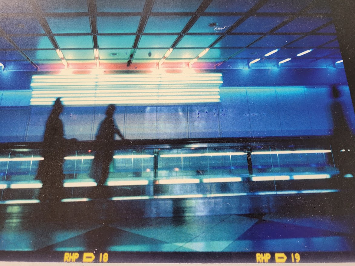 Silhouette d'un couple sur le trottoir roulant à l'aéroport de Munich, image à dominance bleue par Michael Joseph