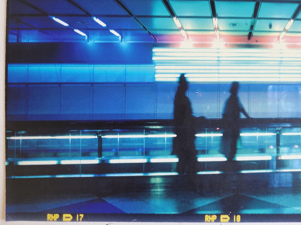 Silhouette d'un couple sur le trottoir roulant à l'aéroport de Munich, image à dominance bleue par Michael Joseph