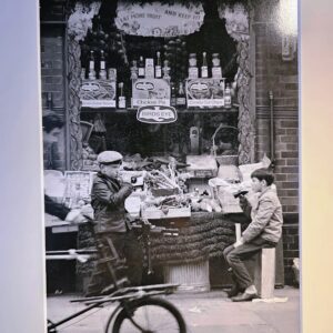Boys drinking coke, under "eat more fruit and keep fit" sign, sixties photo taken in East End London by Michael Joseph