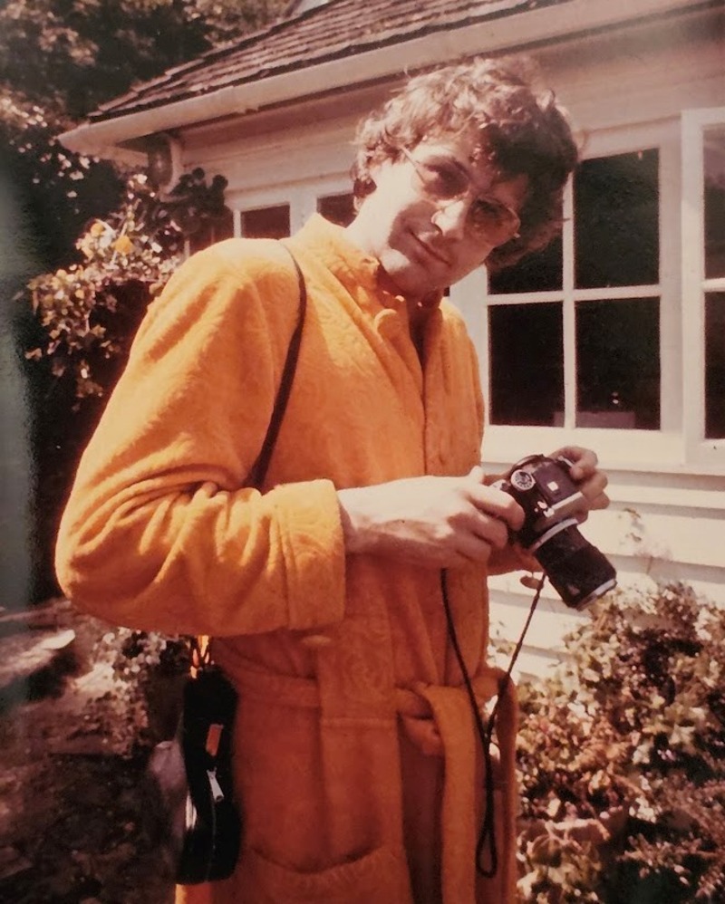 Michael Joseph wearing an orange shirt and holding a camera